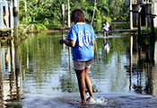 Woman walks through flooded street, water up to her ankles, 2-story wooden buildings on either side of street