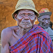 Elderly African man seated outside looks directly at camera