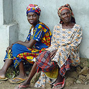 Two older women in Nigeria seated outdoors on a pile of rocks