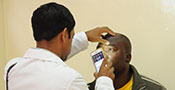Medical worker examines patient’s eye in exam room using smartphone.