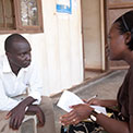 Female researcher takes notes while interviewing male study participant who is sitting across from her outdoors