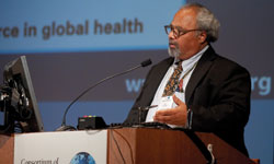 PHOTO: Ambassador Eric Goosby speaks into a microphone at a podium, with a small segment of a slide projected in the background.