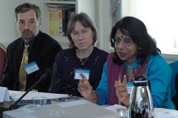 PHOTO: A woman in a bright blue sari gestures with her hands while speaking, seated at a table behind a microphone