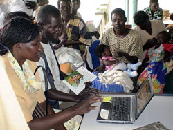 A group of Africans gather around a computer while one woman uses it.