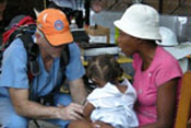 PHOTO: Hatian woman holding young child in her lap seated next to male doctor, squatting