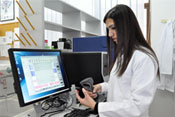PHOTO: Woman in lab coat in front of computer screen uses hand-held scanner attached to desktop computer