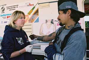 Woman wearing plastic gloves holds the arm of a man in front of a mobile health clinic.