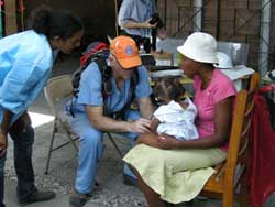 PHOTO: Hatian woman holding young child in her lap seated next to male doctor, squatting