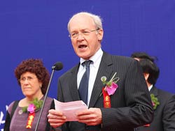 Photo: Dr Auchincloss speaks into a microphone at a podium two, woman and man stand in front of blue background