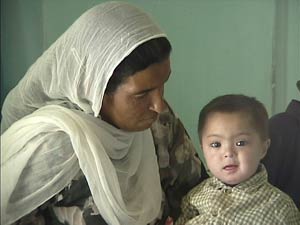 Pakistani woman seated watches a boy toddler on her lap