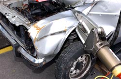 Silver metal on a damaged vehicle is lifted by a mechanical metal arm