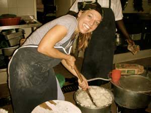 Dr. Elizabeth Vaughan, smiling, stirs large metal pot full of white porridge with large wooden spoon