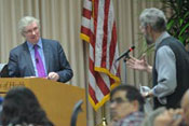 Lord Nigel crisp at podium listens as man speaks into microphone from  audience