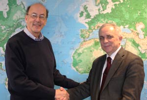 Dr Roger I Glass shakes hands with Dr. M.V. Ugrumov in front of world map