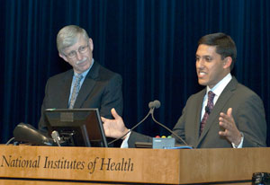 Dr. Rajiv Shah speaks into microphone at podium, Dr. Francis Collins stands next to him