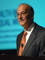 Dr. Roger I Glass speaking at podium, slide projected in background