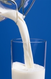 milk from a glass pitcher being poured into a glass with a blue background. Photo: National Dairy Council.