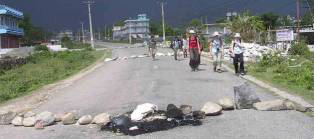 makeshift roadblock in Nepal with rocks going across sections of a long road, people walk in the road