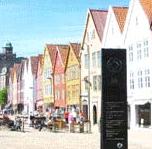 The UNESCO Heritage Site in Bergen, Norway. There is a row of colorful, quaint-looking buildings with people sitting outside cafe style.