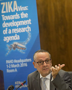 Dr Marcos Espinal, speaks into microphone in a conference room, sign on Zika Virus in the background