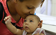 In Brazil, a mother kisses baby, who has a smaller than usual head