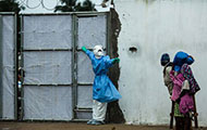 Photo by Morgana Wingard, courtesy of USAID, Healthcare worker outside Ebola clinic in full protective gear covering holds gate