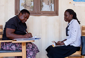 By Richard Lord for Fogarty/NIH. Researcher taking notes while interviewing research subject outdoors.