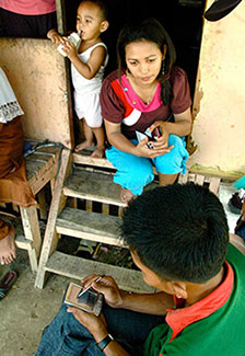 man seated enters data on a handheld device, woman faces him sitting on wooden steps in doorway