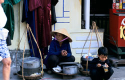 Photo: a Vietnamese woman and child crouche next to pots on the sidewalk