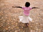 young girl in skirt twirls on brick-paved street, arms fully extended