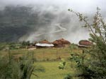 Group of four huts on hillside, mist rises above them, seen from higher on hill