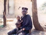 Man seated on dusty ground, infant in his lap