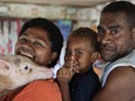 Small pig rests head on woman’s shoulder, child and man stand behind woman