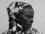 black and white photo of profile of older Tanzanian woman wearing flowered head scarf and top