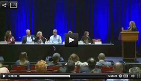 Screen capture of webcast of a speaker on a stage at a podium engaging with 6 panel members
