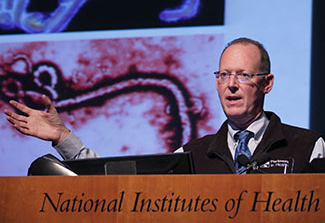 Paul Farmer speaking at a podium at NIH, slide projected in the background