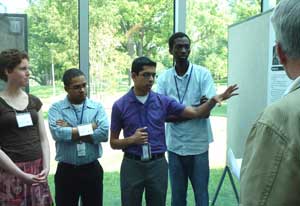 Sujal Parikh points to a mounted conference poster, four peers, all wearing conference badges, look on