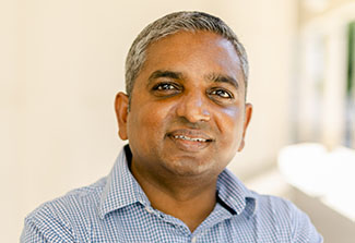 The photo shows a headshot of Dr. Deshen Moodley, wearing a blue gingham shirt.