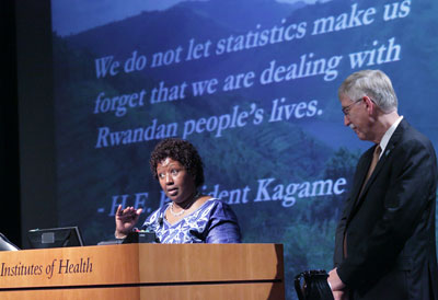 Dr. Agnes Binagwaho speaking at a podium, Dr. Francis Collins looks on, slide projected in the background