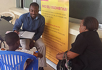 Dr. Emmanuel Balandya talks with young patient and parent who are seated across from him