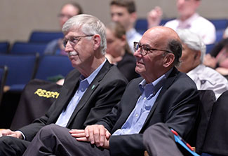 Dr. Francis S. Collins and Dr. Roger I. Glass attentively watch the Barmes Global Health Lecture from seats in the auditorium.