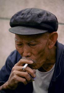 Older Chinese man smokes a cigarette