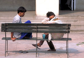 Two men seated on a bench in an outdoor courtyard face each other