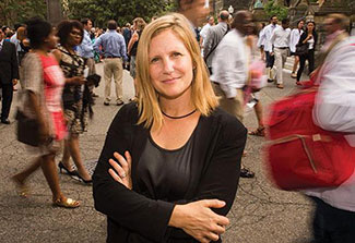 Dr. Emily Mendenhall poses on a street outdoors, many pedestrians walk on a busy street in the background.