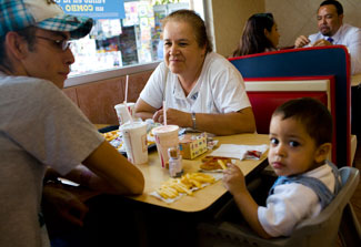 Woman, man and young child seated at booth in fast food restaurant with drinks and fries on table
