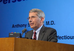 Dr. Anthony S. Fauci speaks into microphone at a podium, slide projected in background