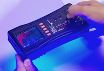 Close up of hands holding FDA Counterfeit Detection Device-3 CD-3, black electronic box with many buttons emits glow on bottom