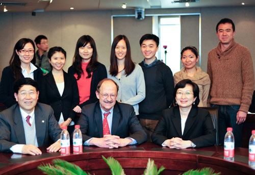 NCI Director Dr Harold Varmus seated at conference table between two officials, seven younger scientists stand behind