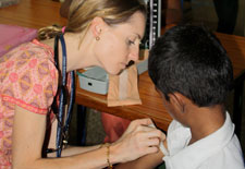 Lucy Horton, wearing stethoscope, holds and observes arm of child patient