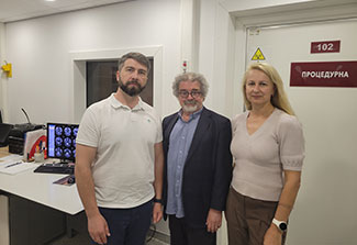 Three scientists stand facing the camera in a Kyiv radiology clinic. From left to right, Ukrainian scientist, Dr. Oleksiy Omelchenko, wears a tan shirt and dark slacks, Dr. Israel Liberzon wears a navy suit over an open-neck blue shirt and Dr. Tetiana Nickelsen wears a beige blouse over tan slacks.
